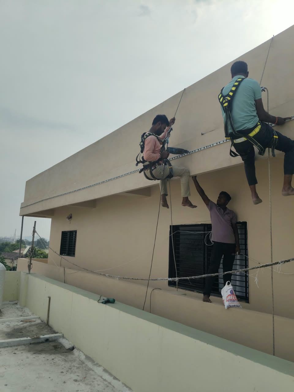 Two installers in safety harnesses fixing invisible grill track to a parapet
